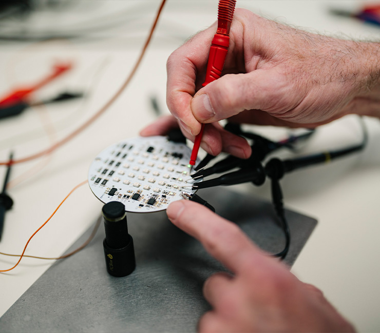 Techniker misst elektrische Signale auf einer Leiterplatte mit einem Prüfgerät im Elektroniklabor von DRD Automation