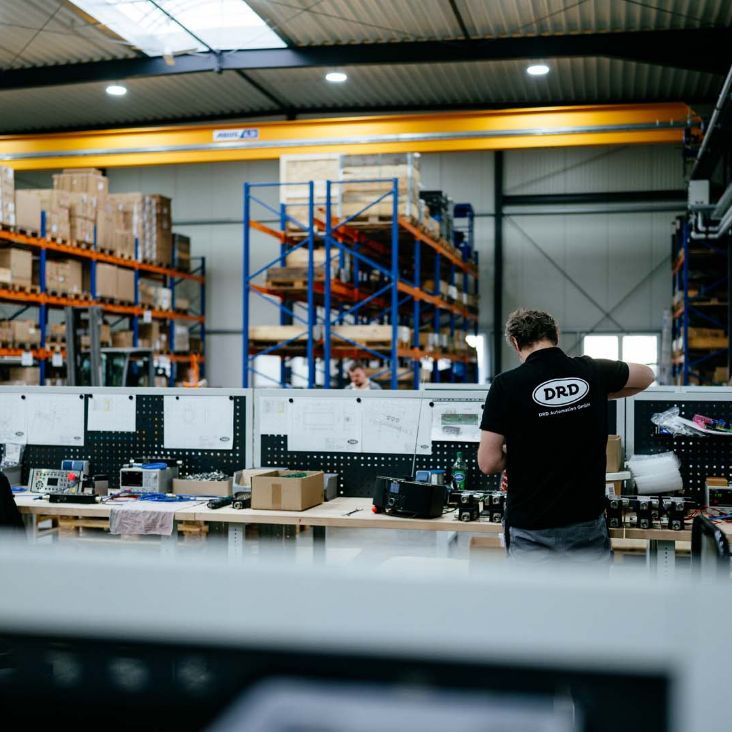 Blick in die Produktionshalle von DRD Automation mit Mitarbeitendem zwischen Werkbänken und Regalen