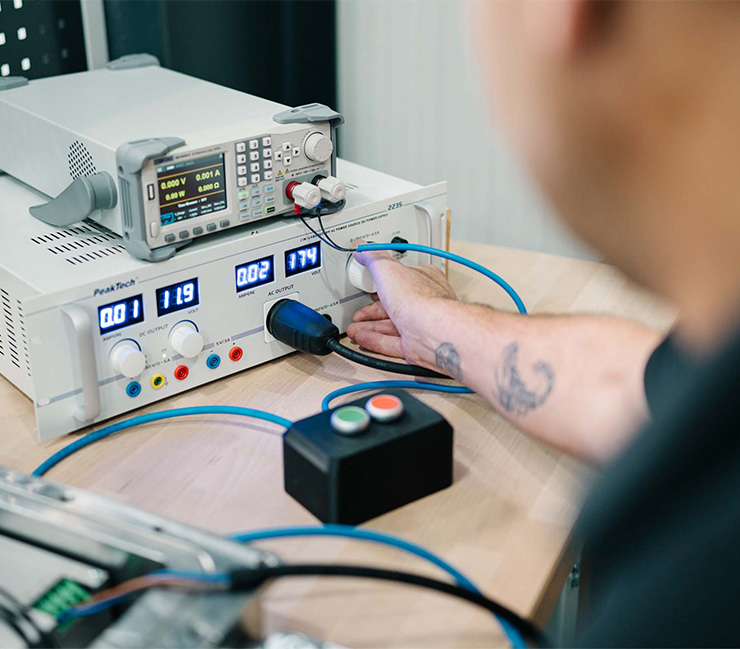 Mitarbeiter testet elektronische Komponenten mit Messgeräten und Netzteilen am Prüfstand von DRD Automation