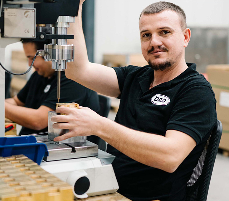 DRD-Mitarbeiter repariert an seinem Tisch, schaut in die Kamera